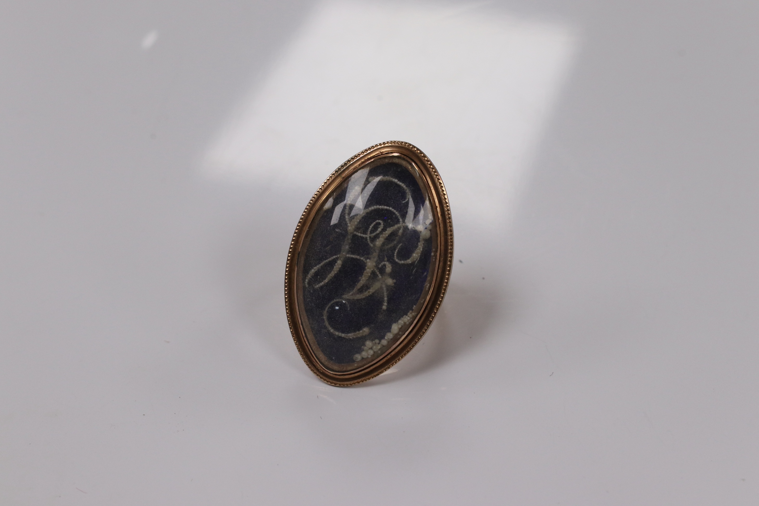 A George III yellow metal, enamel and simulated seed pearl set initialled oval mourning ring, with engraved inscription, 'Isaac Sparks ob. 17th Jan, 1788 ae. 60' size G/H, gross weight 7.6 grams. Condition - poor